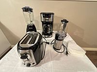 Group shot of toaster, blender, coffee maker, kettle, grinder and filters on table