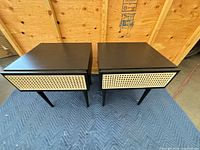 Pair of black nightstands with rattan fronts on blue moving blanket