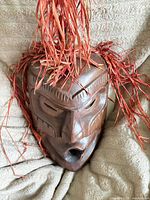 Front view of carved wooden mask with red raffia hair