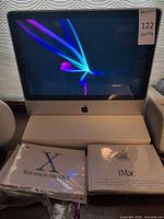 iMac front view powered on with manuals in foreground