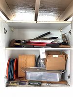 Overview of cabinet shelf with roasting pan, cord reel, hand tools, boxes