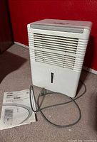 Front view of dehumidifier with manual and power cord visible