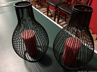 Pair of black wire candle holders each containing a red pillar candle