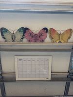 Three butterfly plaques and calendar board on shelving
