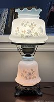 Full view of lamp with both globes lit, showing floral decoration and blue ruffled top