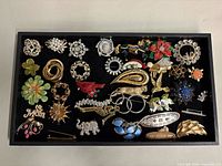 Overall view of 32 assorted vintage costume brooches laid in tray