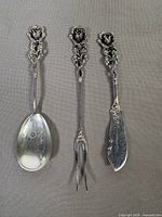 Three sterling utensils—spoon, fork, knife—displayed front