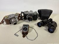 Group shot showing both cameras, light meter, binoculars, and Yashica case cover