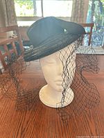 Front view of black straw tilt fascinator with veil displayed on mannequin head