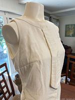 Front upper view of ivory silk sleeveless dress on mannequin showing fabric texture and armholes