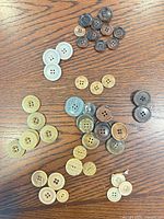 Overview of all assorted beige and brown plastic 4-hole buttons spread on wooden surface