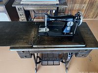 Top view of Singer treadle sewing machine set into wooden cabinet, showing drawers and cast iron base