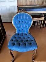 Front view of Victorian-style blue velvet tufted parlour chair showing carved floral crest and cabriole legs