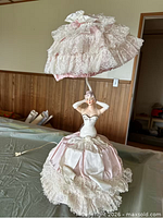 Front view of lady figurine lamp showing pink satin and lace gown, parasol shade, cord visible