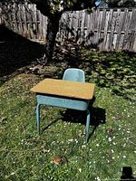 Front angled view of desk-chair showing wood laminate desktop, blue-teal frame and molded plastic seat
