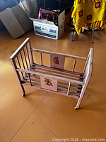 Overall view of pink wooden doll cradle showing slatted sides, decals, and caster wheels