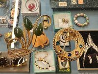 Two brooches on glass surface: leaf spray with green cabochons and round rhinestone wreath