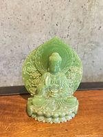 Front view of small green Buddha statue with lotus base and floral halo