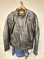 Front view of black leather jacket hanging, showing asymmetrical zipper, pocket, quilted shoulders