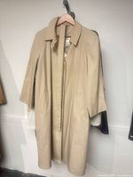 Front view of beige trench coat on hanger showing overall style and length