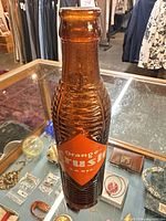 Full view of amber ribbed Orange Crush bottle inside display case