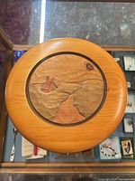 Top view of circular wood plaque showing carved landscape scene, grain and inlay ring