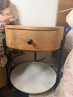 front view of round nightstand showing drawer, marble shelf, metal legs