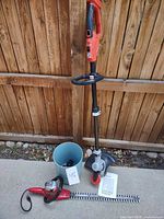 Full view of string trimmer, hedge trimmer, bucket with batteries and chargers, manual visible