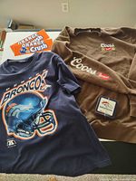 Group shot of all items: tee, sweatshirt, coasters, stickers