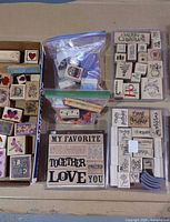 Overview of lot showing cardboard tray of colorful wood stamps, two zip bags with loose stamps and rollers, and three plastic clamshell storage cases