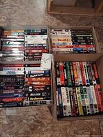 Three boxes filled with assorted VHS tapes showing spines with various movie titles