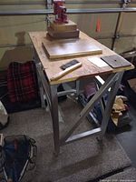 Overall view of metal workbench with plywood top, vise, brush, metal plate, casters visible