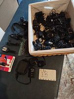 Basket containing numerous black wall AC adapters plus several chargers and cords laid out
