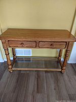 Full front view of oak console table showing two drawers, turned legs and glass shelf