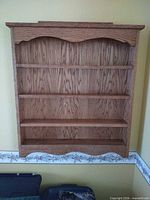 Front view of oak veneer wall shelf showing four shelves and scalloped top and bottom