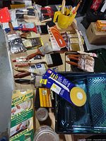 Tabletop view of brushes, rollers, trays, caulk tape, small paint tins