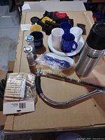 All items laid out showing thermos, coffee pot, saw, clothespins, mugs, plate, bowl, cup, shaker, water-bottle holders