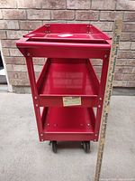 Front view showing three red metal shelves and caster wheels