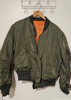 Front view of olive green Alpha Industries bomber jacket on hanger
