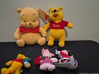 Two Winnie the Pooh plush toys plus three plush Christmas ornaments displayed on table