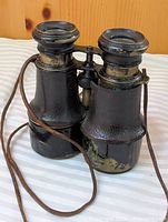 Front view of antique black binoculars showing leather wrap and strap