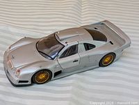 Left front and side view of silver Mercedes-Benz CLK GTR die-cast model with gold wheels