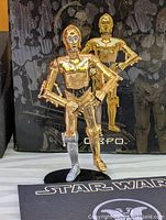 Front view of metal C-3PO figure on stand with box backdrop