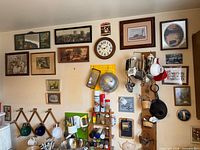 Overall view of kitchen wall showing clock, framed prints, pegboards, spice shelves, mug racks