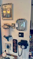 Full view of wall and table showing phone, clock, floral print, shelf, vase, plaques and figurine