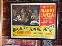 Full view of framed lobby card mounted on brick wall