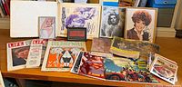 Overall view of framed photos, magazines, sheet music binder and postcards on table