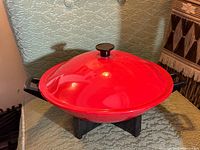 Overall view of red electric wok on black base, showing lid and handles