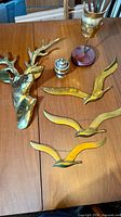 Brass stag head, three brass seagulls, brass face goblet on wood base, small lidded brass vessel displayed on tabletop