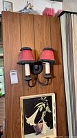 Wall section showing black metal two-arm sconce with red shades; framed plant print below
